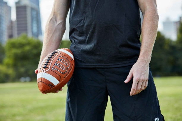 Person holding a Wilson GST Prime football with grip-enhancing stitches and high visibility accents outdoors